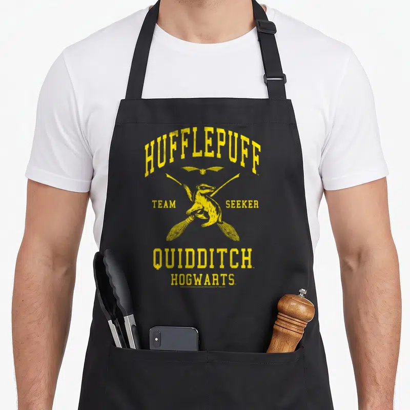 Hallow hufflepuff apron - Yellow badger on broomstick with HUFFLEPUFF TEAM SEEKER QUIDDITCH HOGWARTS distressed text — shown on a black cotton canvas apron against a white background