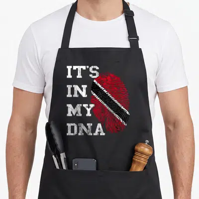 Dna trinidadian apron - It's in my dna text beside a red black and white fingerprint containing a flag pattern — shown on a black cotton canvas apron against a white background