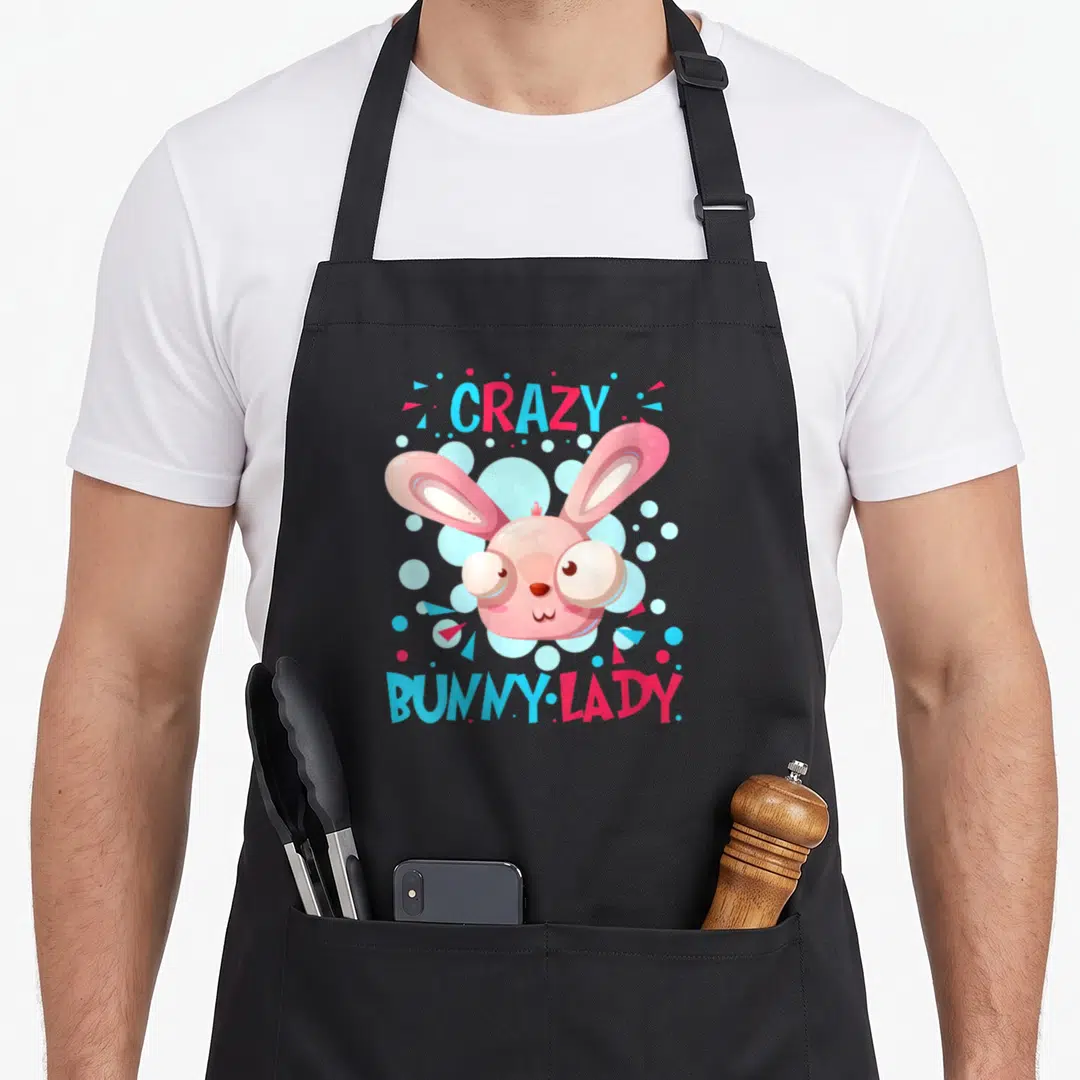 Rodent easter bunny aprons - Pink cartoon bunny head with CRAZY BUNNY LADY text and blue circles — shown on a black cotton canvas apron against a white background