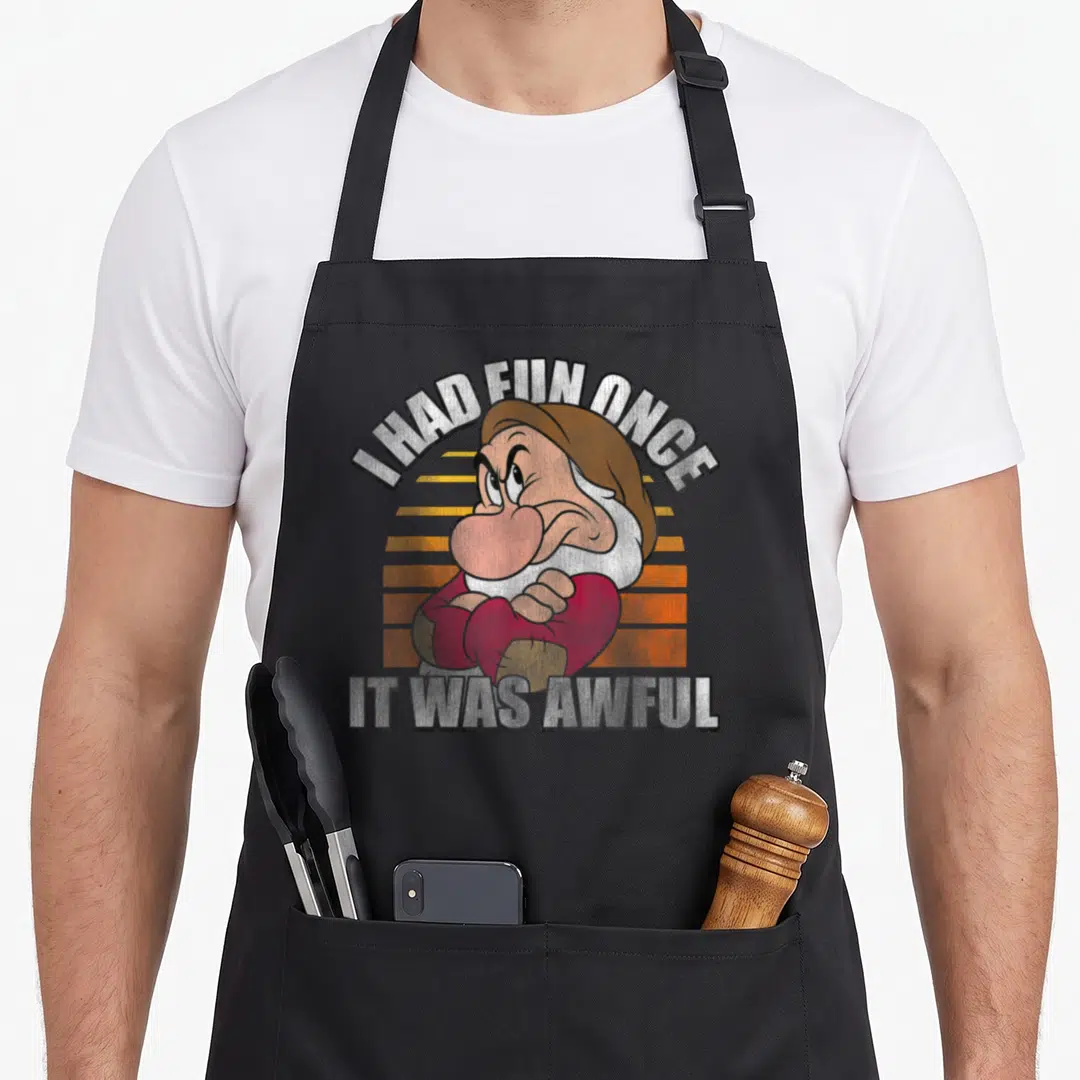 Once snow white apron - Grumpy cartoon character with I Had Fun Once It Was Awful text over striped sunset — shown on a black cotton canvas apron against a white background