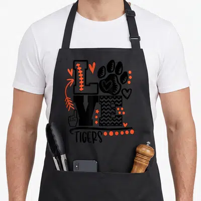 Tiger football apron - LOVE typography with paw print O and TIGERS text in black and orange — shown on a black cotton canvas apron against a white background