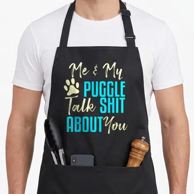 Puggle pug dog apron - Cyan and cream text reading Me & My PUGGLE Talk SHIT ABOUT You with paw print — shown on a black cotton canvas apron against a white background