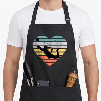 Funny volleyball apron - Retro heart with striped teal yellow orange background and black diving volleyball player — shown on a black cotton canvas apron against a white background