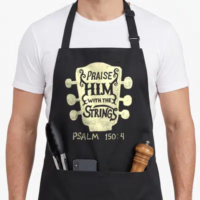 Guitarist christian music apron - Beige guitar headstock with grey Praise Him With The Strings text and Psalm 150:4 — shown on a black cotton canvas apron against a white background
