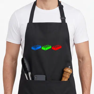 Construction block & apron - Three toy bricks in blue, green, and red arranged horizontally in a minimalist style — shown on a black cotton canvas apron against a white background