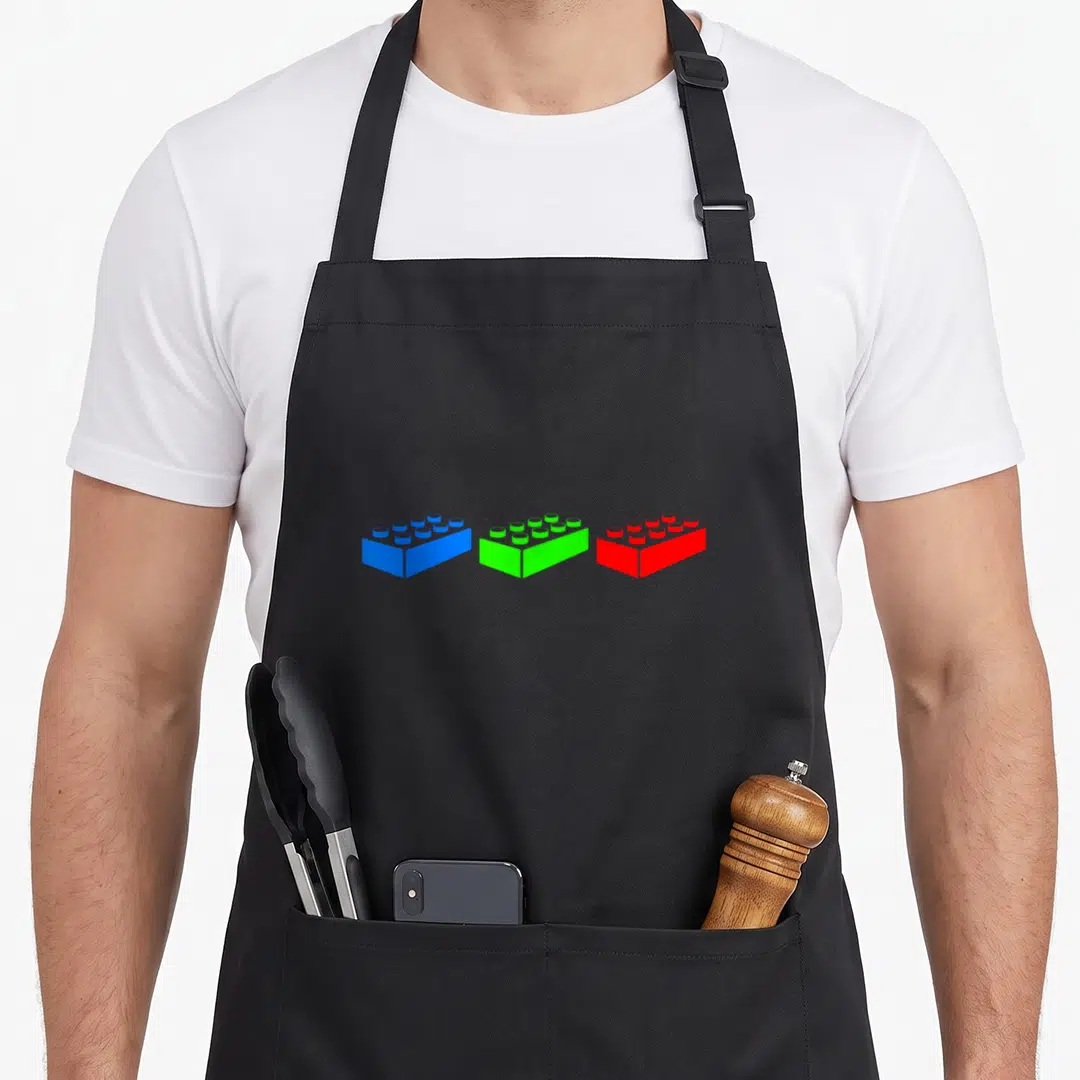 Construction block & apron - Three toy bricks in blue, green, and red arranged horizontally in a minimalist style — shown on a black cotton canvas apron against a white background