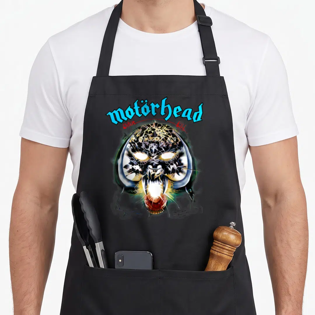 Mot band apron - Cartoon monster head with motörhead text arched above and OVER KILL on sides in blue red and black — shown on a black cotton canvas apron against a white background