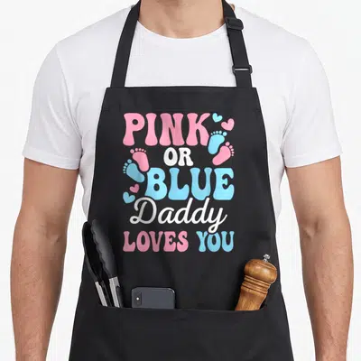 Blue gender reveal daddy apron - Stacked pink white and blue text reading pink or blue daddy loves you surrounded — shown on a black cotton canvas apron against a white background