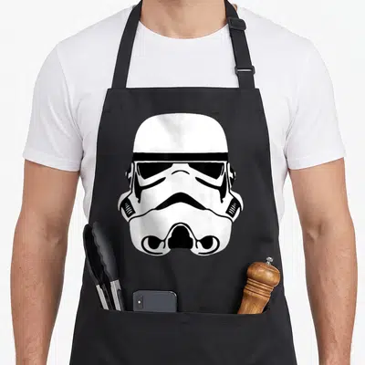 Helmet state trooper apron - Minimalist white and black stormtrooper helmet graphic centered on apron front — shown on a black cotton canvas apron against a white background
