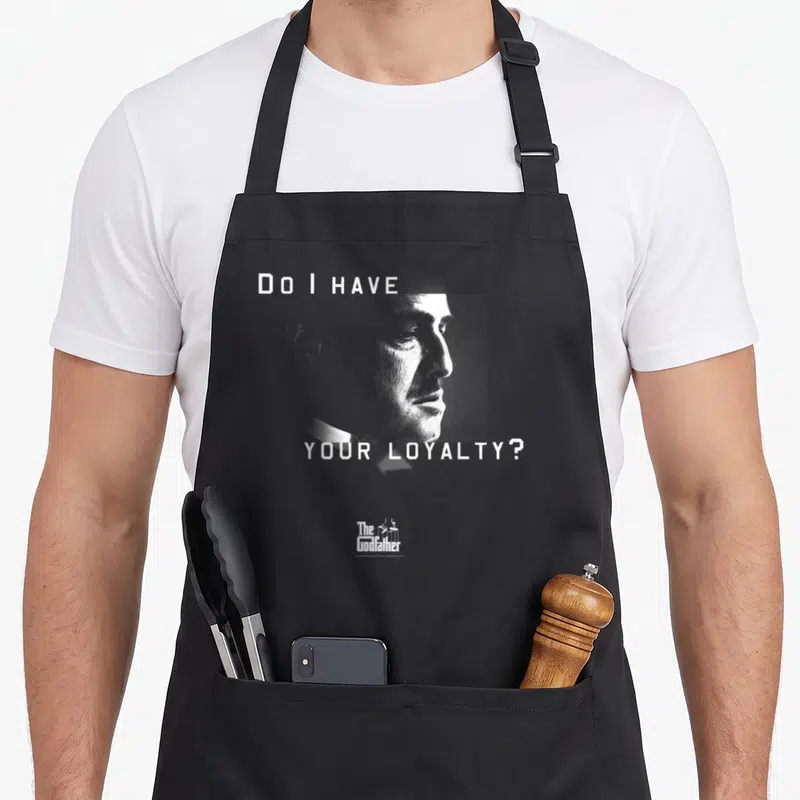 Vito godfather apron - Do I HAVE YOUR LOYALTY text framing a grey minimalist male profile portrait — shown on a black cotton canvas apron against a white background