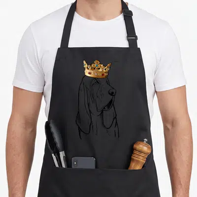 Bloodhound dog wearing apron - Line art bloodhound head with realistic gold crown adorned with red and blue gems — shown on a black cotton canvas apron against a white background