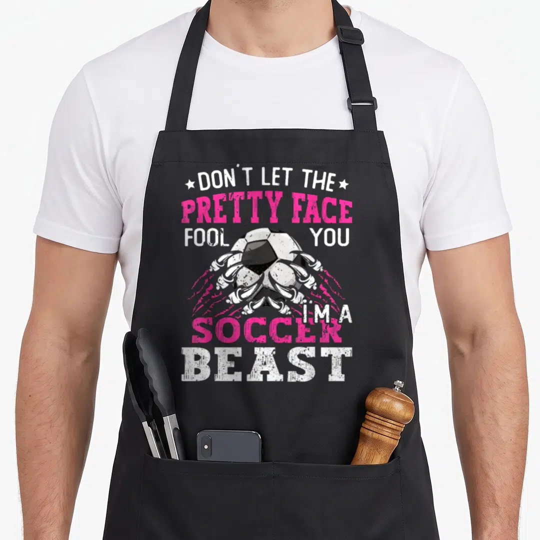 Fool pretty apron - Soccer ball gripped by claws with Don't Let The Pretty Face Fool You I'm A Soccer Beast text — shown on a black cotton canvas apron against a white background