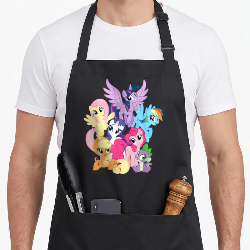 Squad pony apron - Five cartoon ponies and a purple dragon in a pyramid formation with pink, blue, yellow, and purple — shown on a black cotton canvas apron against a white background
