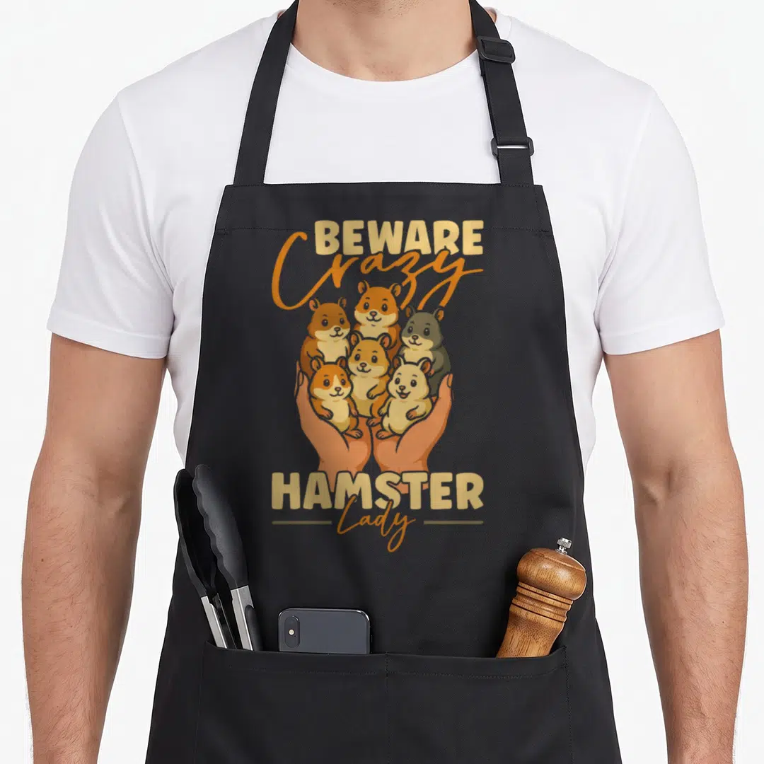 Beware comfort crazy hamster lady apron - Six cartoon hamsters held by two hands with Beware Crazy Hamster Lady text — shown on a black cotton canvas apron against a white background