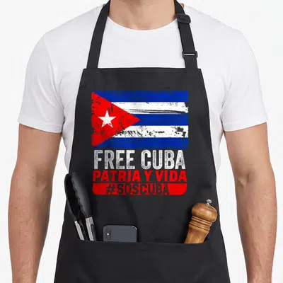 Sos cuba libre apron - Distressed Cuban flag above white and red text reading Free Cuba Patria y Vida hashtag SOScuba — shown on a black cotton canvas apron against a white background