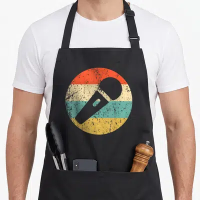 Microphone karaoke apron - Grey microphone silhouette over four horizontal stripes in red beige teal and yellow within — shown on a black cotton canvas apron against a white background