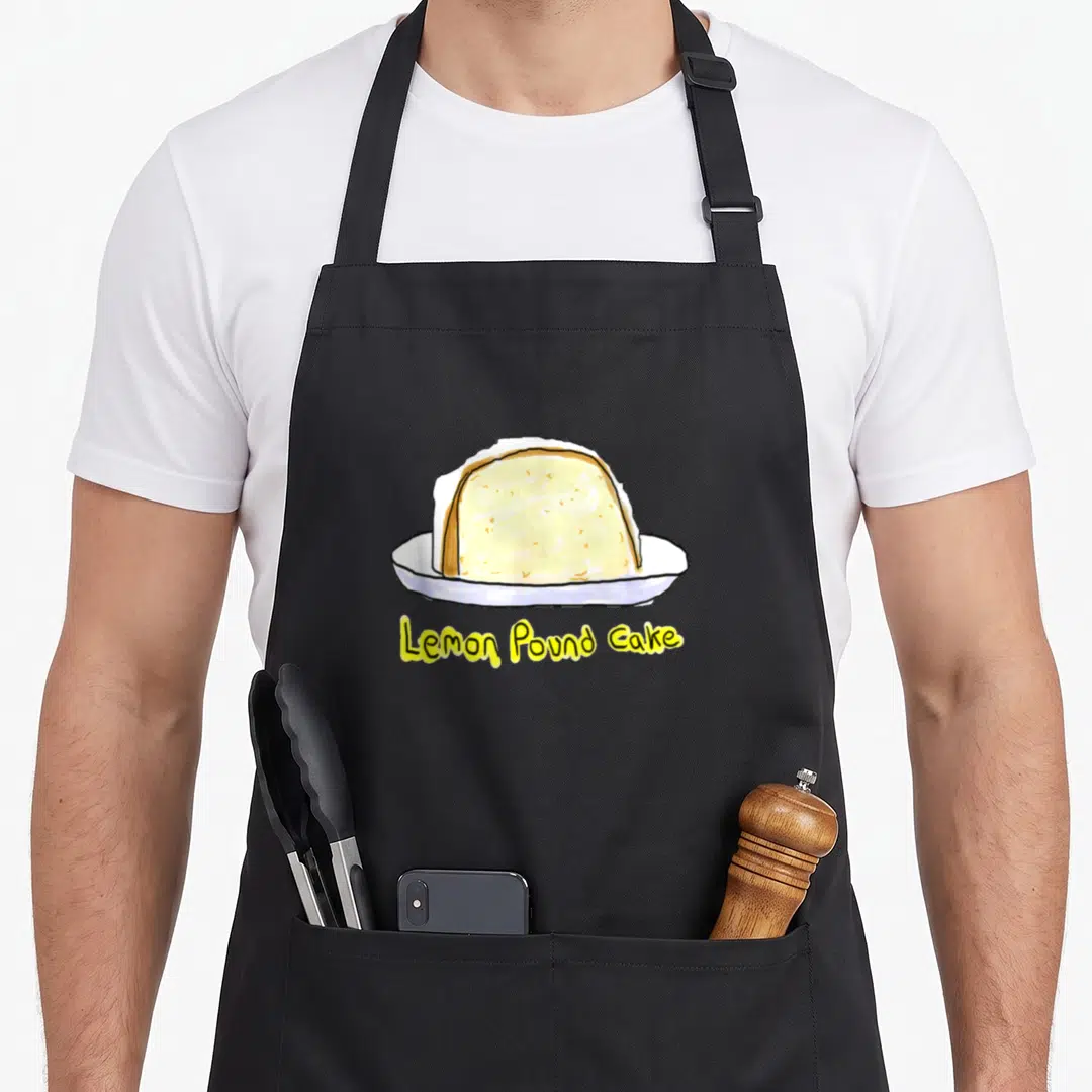 Pound lemon aprons - Cartoon slice of yellow pound cake on white plate with yellow text reading Lemon Pound Cake below — shown on a black cotton canvas apron against a white background