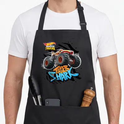 Funny tiger shark apron - Monster truck illustration with HOT WHEELS logo and Tiger Shark text in orange and blue — shown on a black cotton canvas apron against a white background