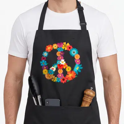 Colorful hippie apron - Peace symbol formed by red blue yellow orange pink and purple cartoon flowers — shown on a black cotton canvas apron against a white background