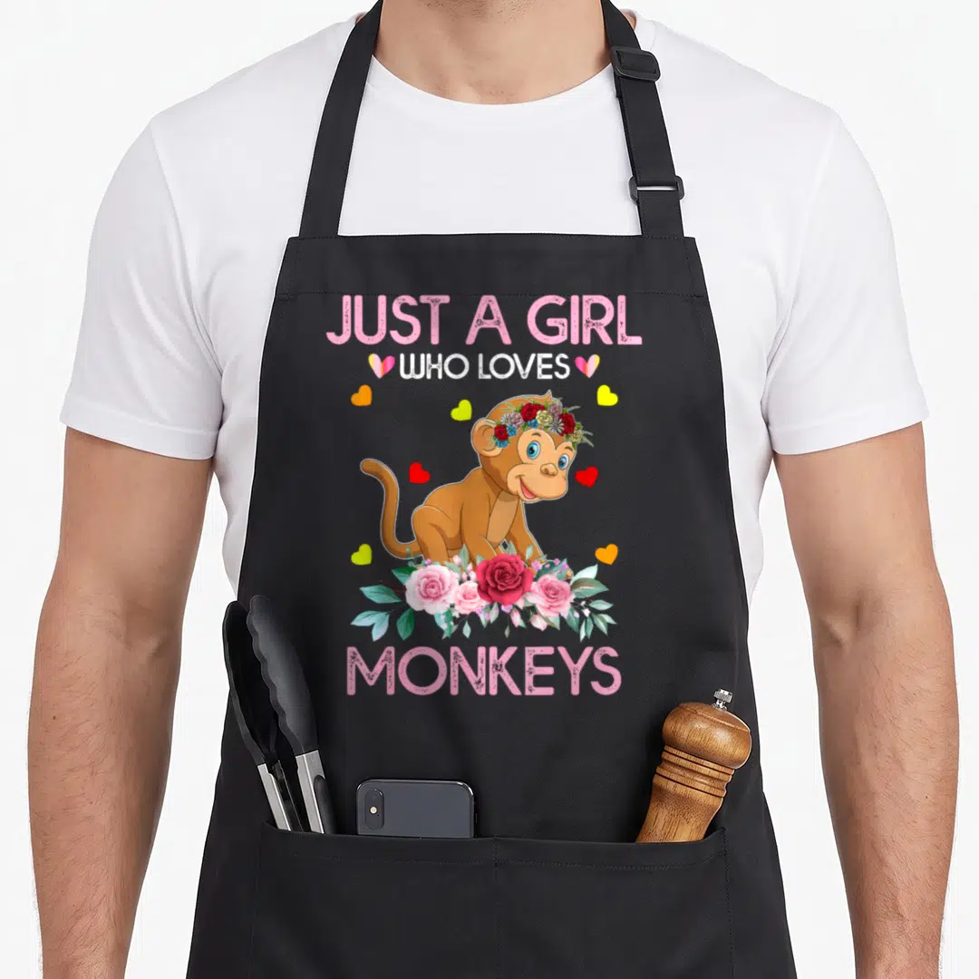 Funny monkey apron - Cartoon monkey with flower crown and roses surrounded by hearts and text Just A Girl Who Loves — shown on a black cotton canvas apron against a white background