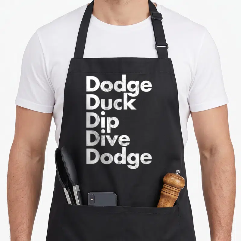 Dive duck apron - Stacked white text reading Dodge Duck Dip Dive Dodge on grey background — shown on a black cotton canvas apron against a white background