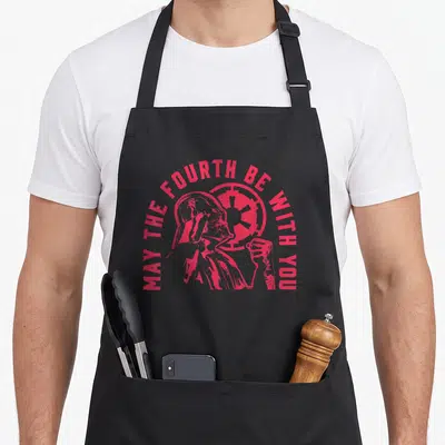 Hue fourth apron - Red arched text MAY THE FOURTH BE WITH YOU over minimalist Darth Vader profile and Imperial emblem — shown on a black cotton canvas apron against a white background