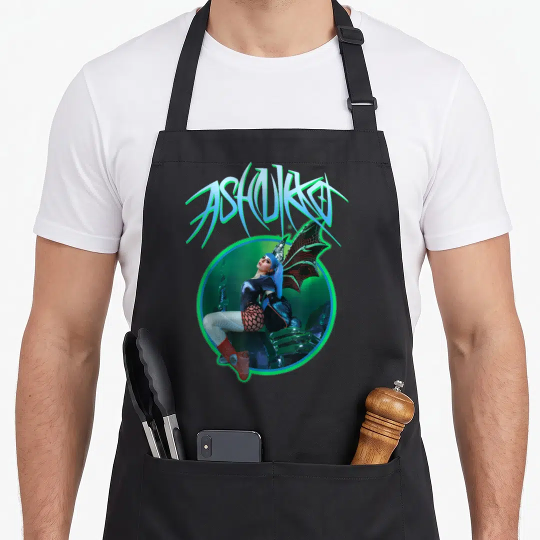 Ashnikko dragon apron - Arched ASHNIKKO text above winged woman in glowing circle with blue, green, red, and black — shown on a black cotton canvas apron against a white background