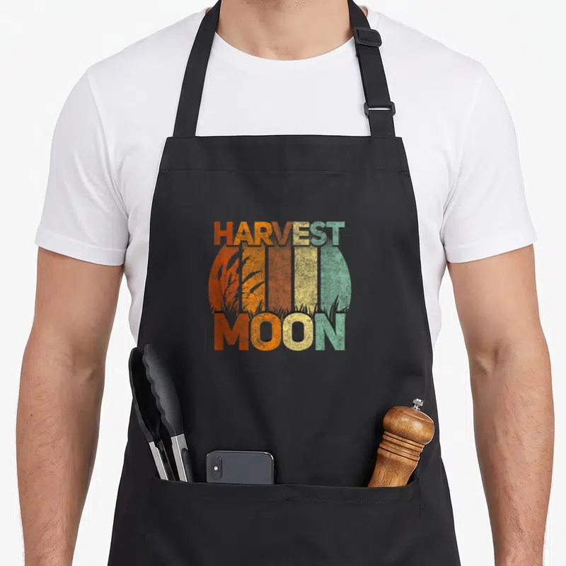 Harvest fall aprons - Retro circular moon with vertical orange yellow green stripes and wheat stalks overlaid — shown on a black cotton canvas apron against a white background