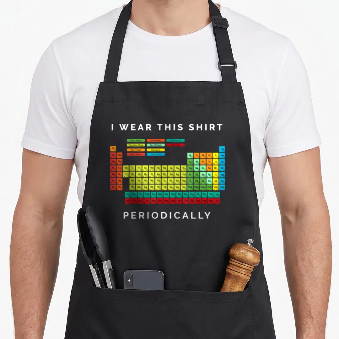 Periodically table apron - Periodic table with I WEAR THIS SHIRT PERIODICALLY text in white green yellow blue red orange — shown on a black cotton canvas apron against a white background