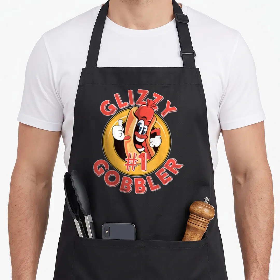 Gobbler hot dog apron - Cartoon hot dog giving thumbs up inside yellow circle with GLIZZY #1 GOBBLER text — shown on a black cotton canvas apron against a white background