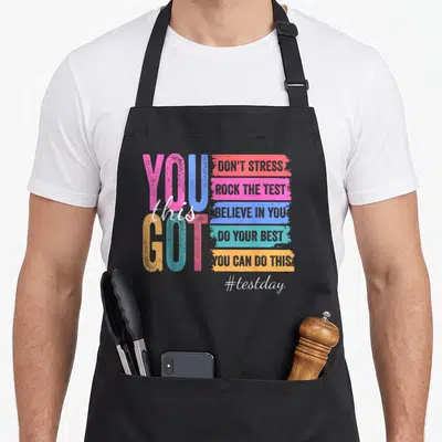 Stress rock test kitchen apron - YOU GOT this motivational text with five colored bars and #testday hashtag — shown on a black cotton canvas apron against a white background