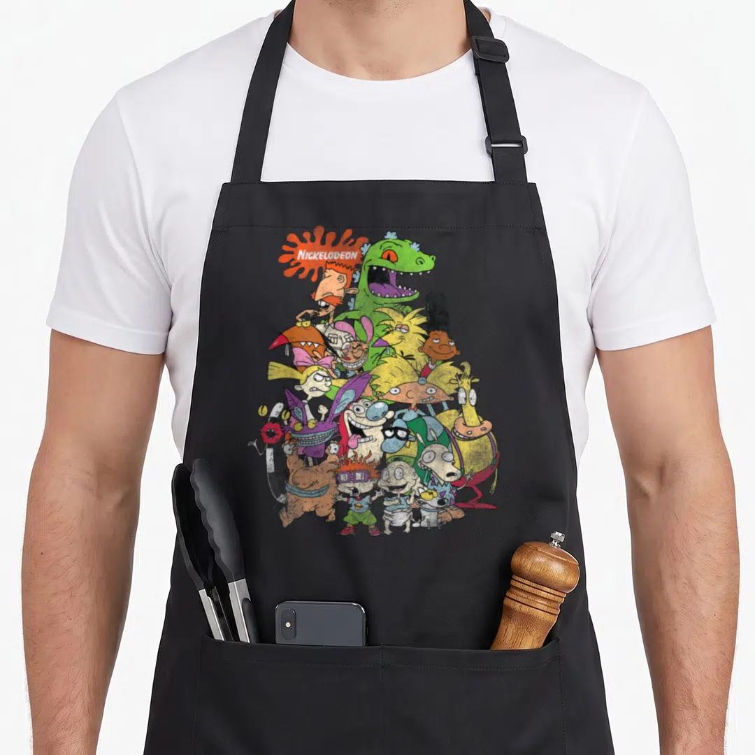 90s cartoon apron - NICKELODEON logo in orange splat above pyramid of cartoon characters in green, yellow, pink — shown on a black cotton canvas apron against a white background