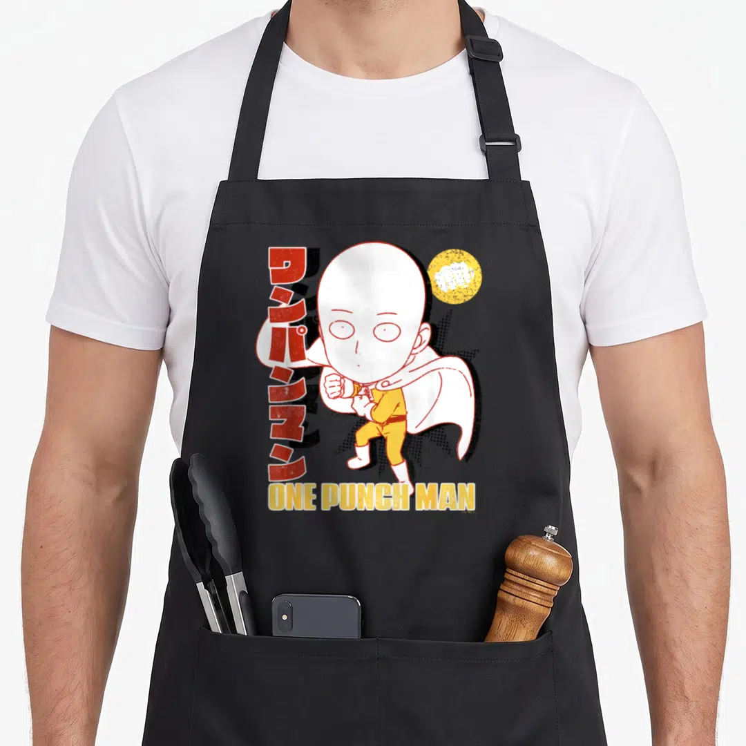 Comic anime apron - Chibi Saitama fist pose with vertical Japanese text and ONE PUNCH MAN lettering — shown on a black cotton canvas apron against a white background