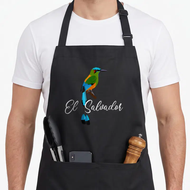 Salvador el cook apron - Colorful blue green orange bird perched on brown branch with white El Salvador script — shown on a black cotton canvas apron against a white background