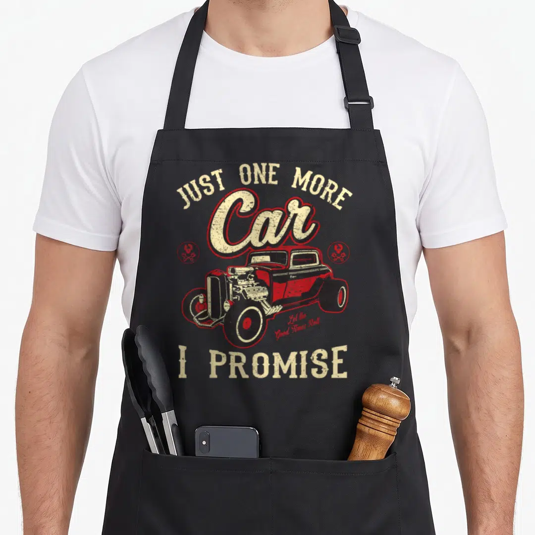 Hot car apron - Distressed hot rod car graphic with Just One More Car I Promise text and gear icons — shown on a black cotton canvas apron against a white background