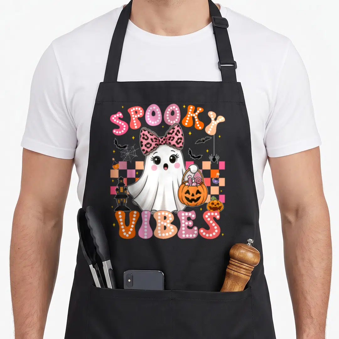 Groovy spooky halloween apron - White ghost with leopard bow holding pumpkin bucket surrounded by bats and marquee text — shown on a black cotton canvas apron against a white background