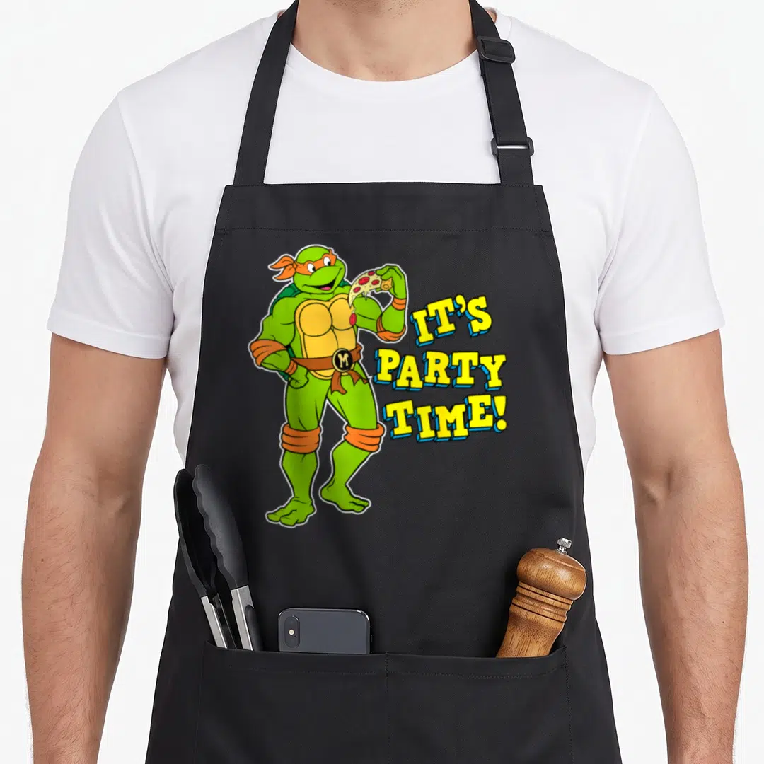 Funny leonardo teenage cooking aprons - Cartoon green turtle with orange mask holding pizza next to IT'S PARTY TIME text — shown on a black cotton canvas apron against a white background