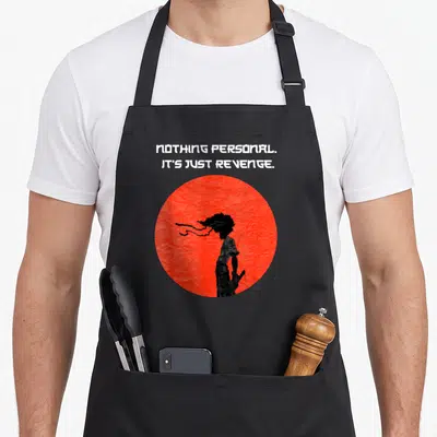 Samurai cartoon apron - Red circle with black silhouette and text NOTHING PERSONAL IT'S JUST REVENGE — shown on a black cotton canvas apron against a white background