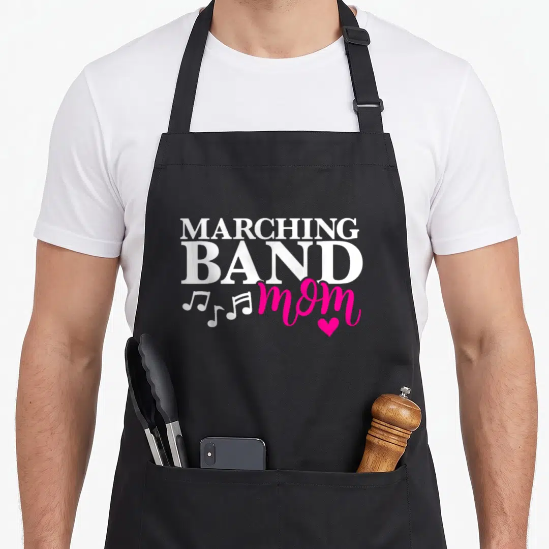 Marching mama apron - White and pink text reading MARCHING BAND mom with musical notes and heart — shown on a black cotton canvas apron against a white background