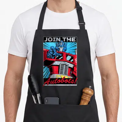Join transformer apron - Optimus Prime pointing forward with Join The Autobots text in red and blue cartoon style — shown on a black cotton canvas apron against a white background