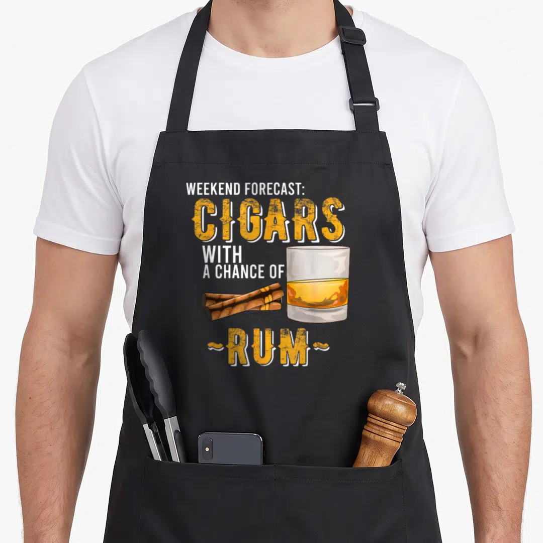 Weekend cigar lovers apron - Stacked text Cigars with Chance of Rum next to glass and two brown cigars lying — shown on a black cotton canvas apron against a white background