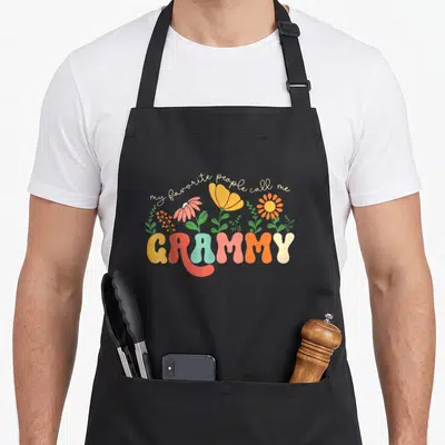 Call mother grammy apron - Floral graphic with my favorite people call me GRAMMY text in cartoon style — shown on a black cotton canvas apron against a white background