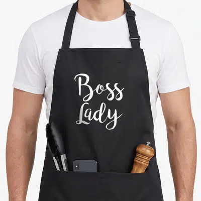 Cute boss apron - White Boss Lady script text stacked vertically on grey background — shown on a black cotton canvas apron against a white background