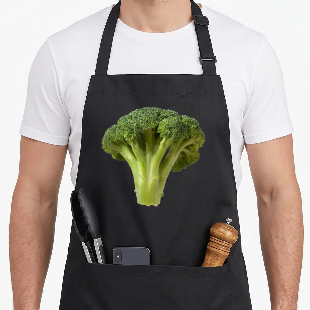 Broccoli halloween apron - Single green broccoli stalk photo print centered on apron front panel — shown on a black cotton canvas apron against a white background