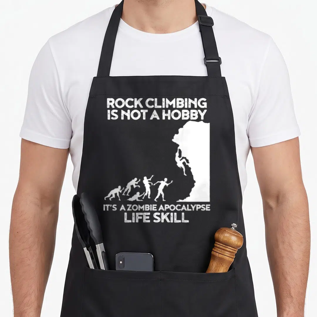 Zombie climbing apron - White text and cliff silhouette with climber and approaching zombies — shown on a black cotton canvas apron against a white background