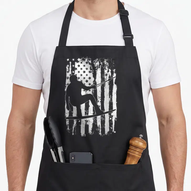 Funny wakeboard wakeboarding apron - Grey wakeboarder silhouette holding rope in front of distressed white and grey — shown on a black cotton canvas apron against a white background