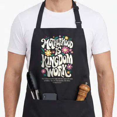 Christian mother's day aprons - Retro text Motherhood Is Kingdom Work with pink yellow purple flowers and Proverbs quote — shown on a black cotton canvas apron against a white background
