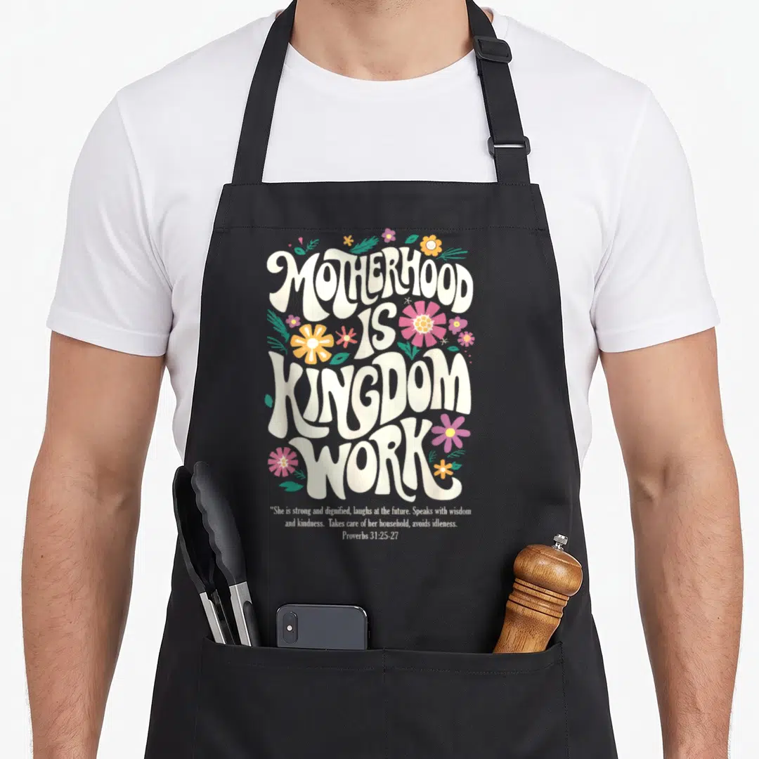 Christian mother's day aprons - Retro text Motherhood Is Kingdom Work with pink yellow purple flowers and Proverbs quote — shown on a black cotton canvas apron against a white background