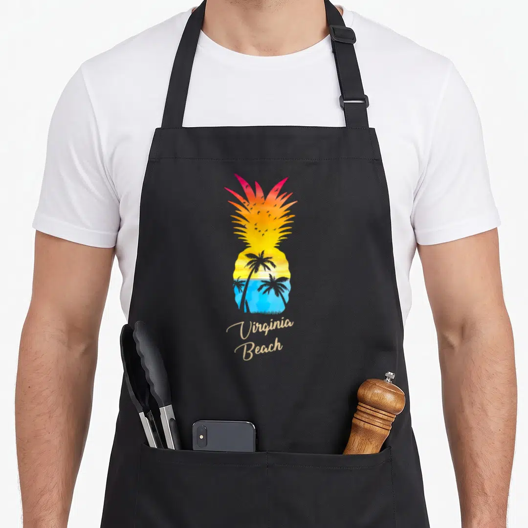 Virginia pineapple apron - Pineapple silhouette with sunset, palm trees, birds, and beige Virginia Beach text — shown on a black cotton canvas apron against a white background