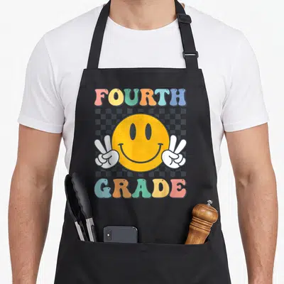 Fourth cute teacher aprons - Retro yellow smiley face with two white peace sign hands and colorful fourth grade text — shown on a black cotton canvas apron against a white background
